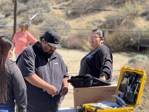 Angela and her crew at TBB 16 splice table Angela looks at her crew explore fiber splicing equipment on a table outdoors on RantenenTown Ranch in the desert-like foothills of Anguana, Califonia