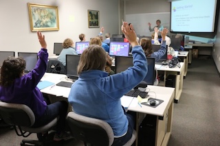A classroom full of seniors raising their hands as the instructor stands at the front of the room