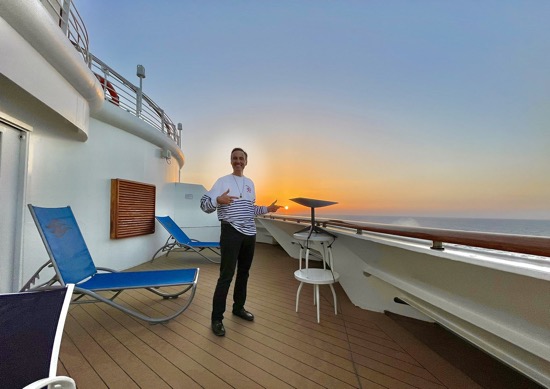 A man stands on the deck of his yacht smiling, standing next to a Starlink satellite fasted to side of yacht