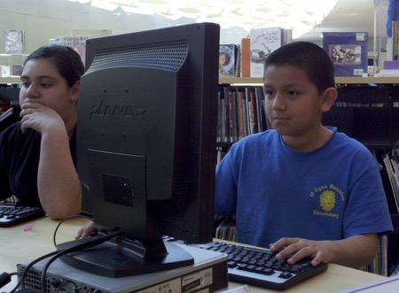Two young students sit in front computers inside library