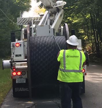 A Lamoille FiberNet in a glowing yellow vest pulls fiber from a spool on the back of a truck
