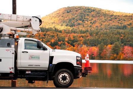 A side view of a NH Electric Coop truck with a forested mountain in background covered in fall foliage