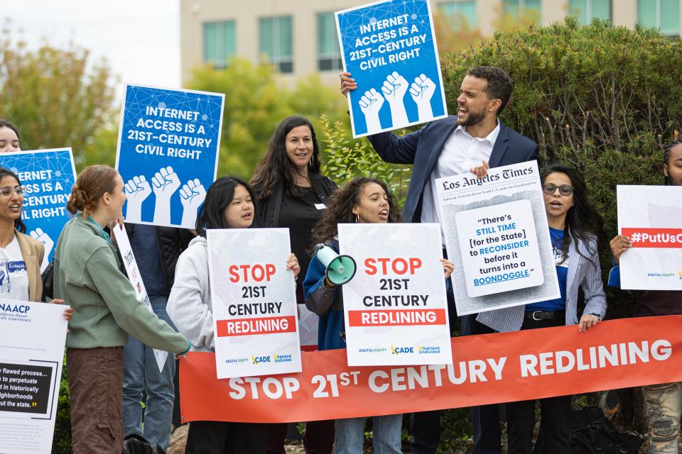 A group of digital equity advocates holds signs that read "Internet Access is a 21st Century Right" and "stop digital redlining" at an outdoor rally