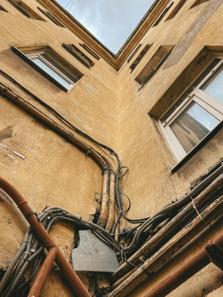A grounds eye view looking up at an old apartment building with old wiring running along the outside of the building 