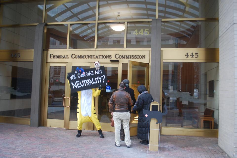 A protestor wearing a cat suit holds a sign in favor of Net Neutrality in front of entrance to FCC building