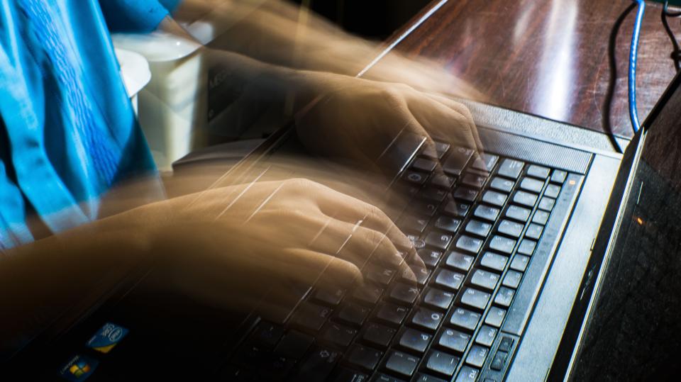 Blurred hands typing fast on a laptop, emphasizing speed and technology.