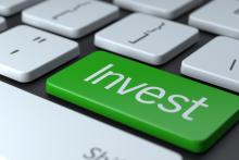 A computer white keyboard focused on a green button with the word "invest" inscribed on it