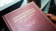 In a library someone is holding a copy of the book "Constitutional Interpretations"