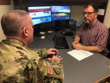 A uniformed veteran sits at desk talking to retirement services rep seated behind a desk