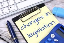 A sticky note reads "changes in legislation" placed near computer keyboard on desk