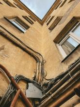 A grounds eye view looking up at an old apartment building with old wiring running along the outside of the building 