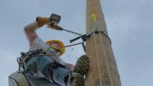 A utility worker drills into utility pole to prepare pole to attach fiber lines