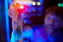 A network engineer in dark room holds up lit fiber strands, illuminating the room with a bluish glow