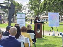 A woman stands at podium to announce project with a map on each side of her