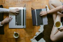 An overhead shot of two women sitting on a wooden floor working on their laptops