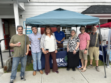 State and local broadband officials stand smiling outside of a tent at the Groton Connectivity Hub opening ceremony