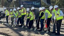 A dozen county officials in safety vests put shovels into ground at groundbreaking ceremony